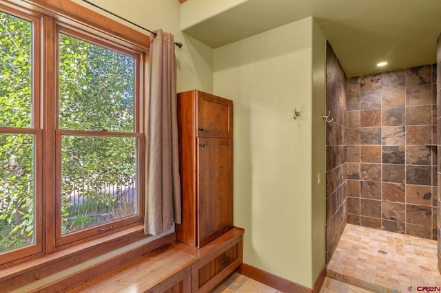 full bath featuring baseboards, a healthy amount of sunlight, and tiled shower