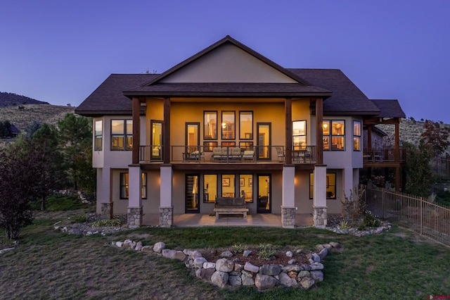 back of house featuring a balcony, fence, stucco siding, a shingled roof, and a patio area