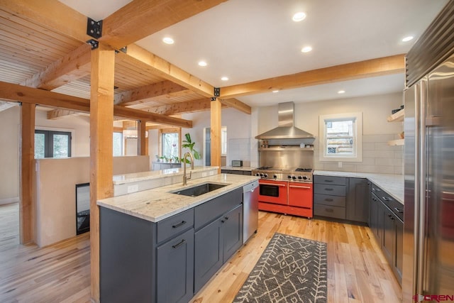 kitchen featuring a sink, light wood-style floors, wall chimney range hood, beamed ceiling, and high end appliances