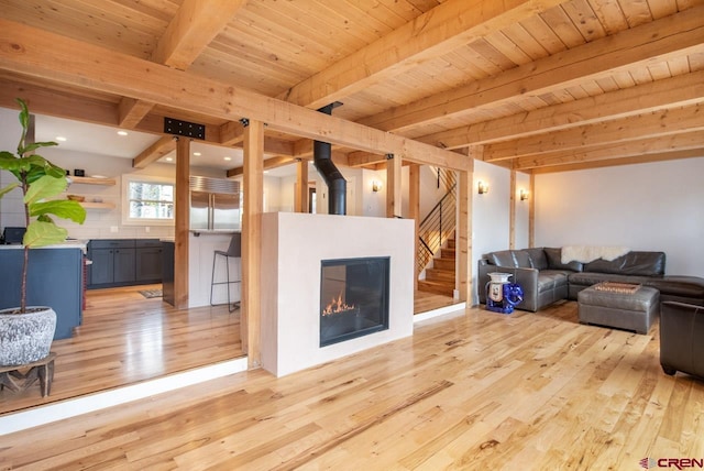 living room featuring stairway, light wood-style floors, a glass covered fireplace, wooden ceiling, and beamed ceiling