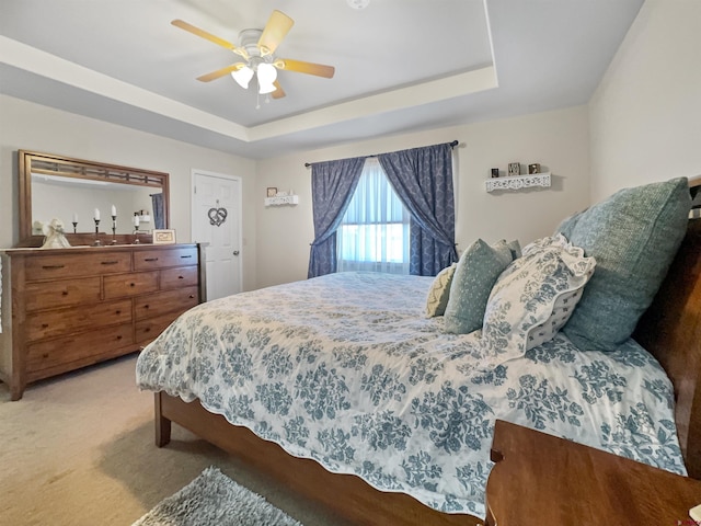 bedroom featuring a tray ceiling, light carpet, and ceiling fan