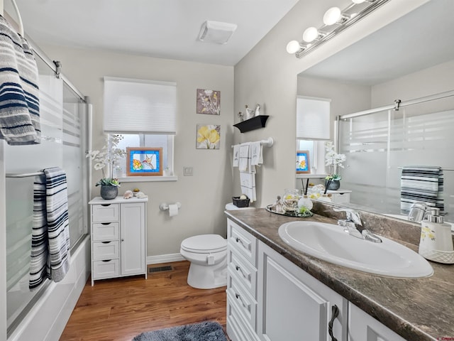 bathroom with visible vents, toilet, enclosed tub / shower combo, vanity, and wood finished floors