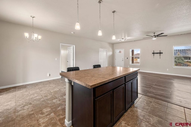 kitchen with dark brown cabinetry, ceiling fan with notable chandelier, a kitchen island, open floor plan, and pendant lighting