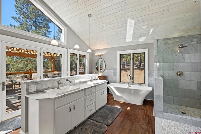 full bath with double vanity, wood finished floors, a sink, walk in shower, and tile walls