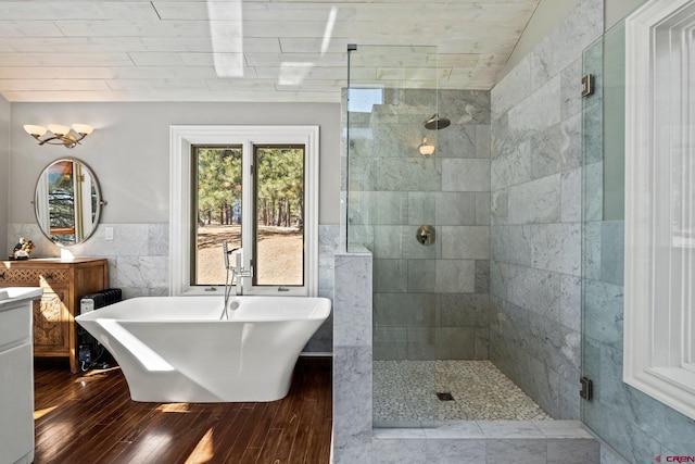 bathroom with tile walls, a soaking tub, a stall shower, vanity, and wood finished floors