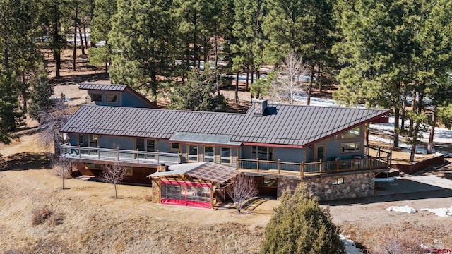 back of house featuring a chimney, metal roof, a standing seam roof, a wooden deck, and stucco siding