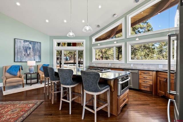 kitchen featuring dark wood finished floors, stainless steel appliances, lofted ceiling, a kitchen island, and dark stone countertops