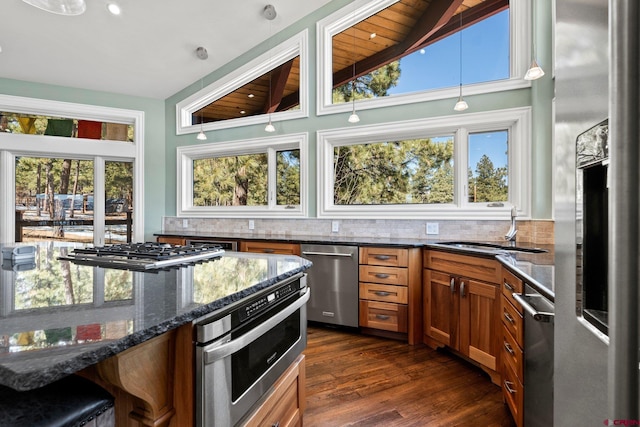 kitchen featuring lofted ceiling, a sink, appliances with stainless steel finishes, brown cabinets, and tasteful backsplash