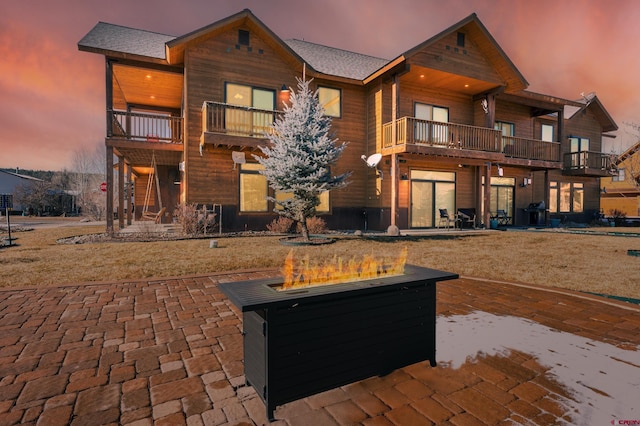 back of house at dusk featuring a patio and a balcony