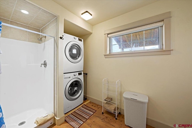 washroom with stacked washer / dryer, laundry area, baseboards, and wood finished floors