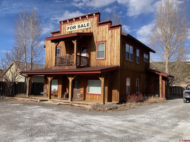 view of front of house featuring board and batten siding, fence, and a balcony