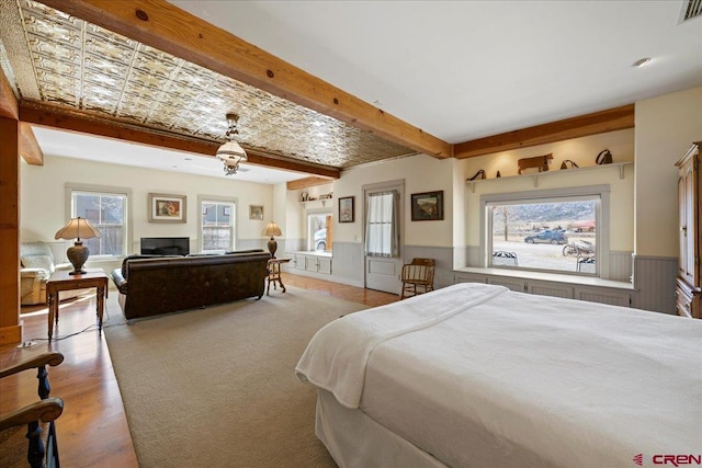 bedroom featuring visible vents, wainscoting, wood finished floors, beamed ceiling, and a fireplace