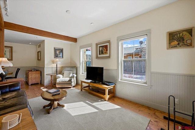 living room featuring a wainscoted wall, beamed ceiling, wood finished floors, and visible vents