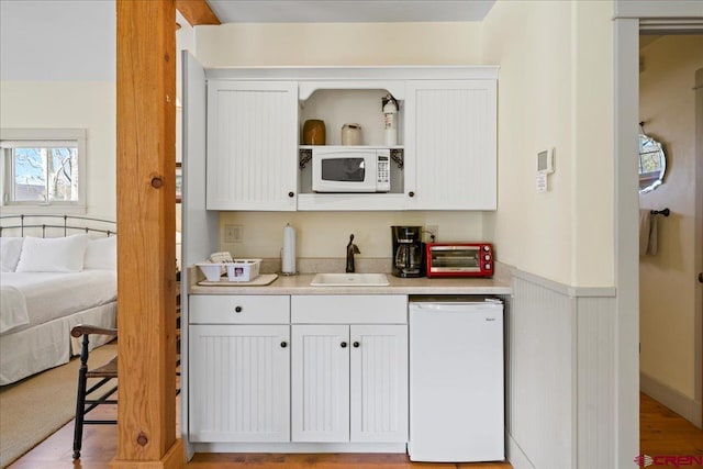 bar featuring a toaster, dishwasher, wainscoting, white microwave, and a sink