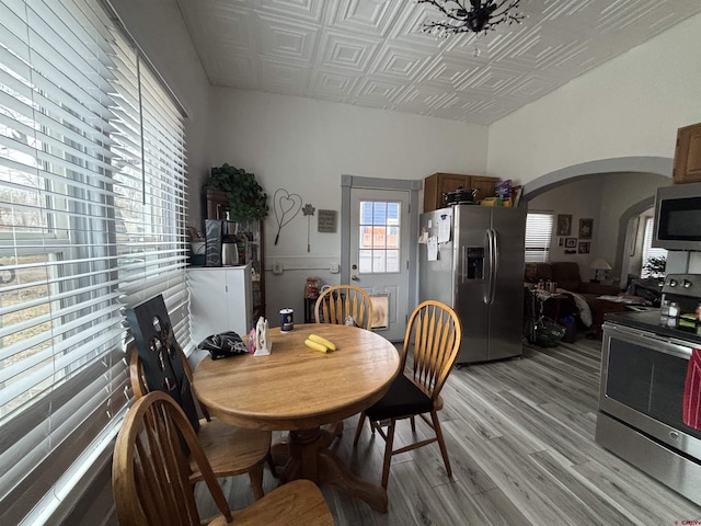 dining space featuring an ornate ceiling, arched walkways, and light wood-style flooring