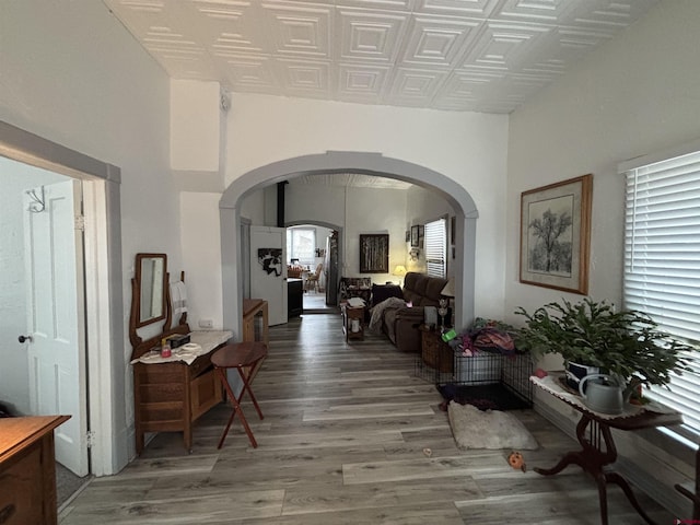 hallway featuring light wood finished floors, an ornate ceiling, and arched walkways