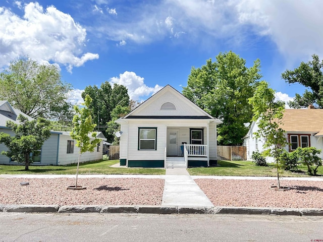 view of front of home featuring covered porch, fence, and a front lawn