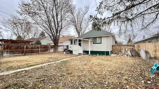 back of property with entry steps, a yard, a chimney, and a fenced backyard