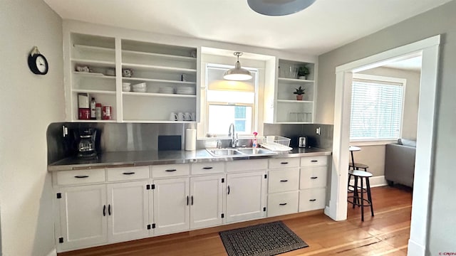 kitchen with decorative light fixtures, light wood-style floors, white cabinetry, open shelves, and a sink