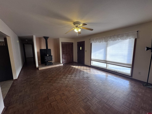 unfurnished living room with a wood stove, ceiling fan, and a textured ceiling