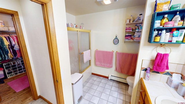 bathroom with a walk in closet, a baseboard radiator, toilet, an enclosed shower, and vanity