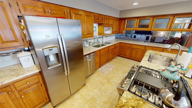 kitchen featuring stainless steel appliances, brown cabinets, a sink, and light stone counters