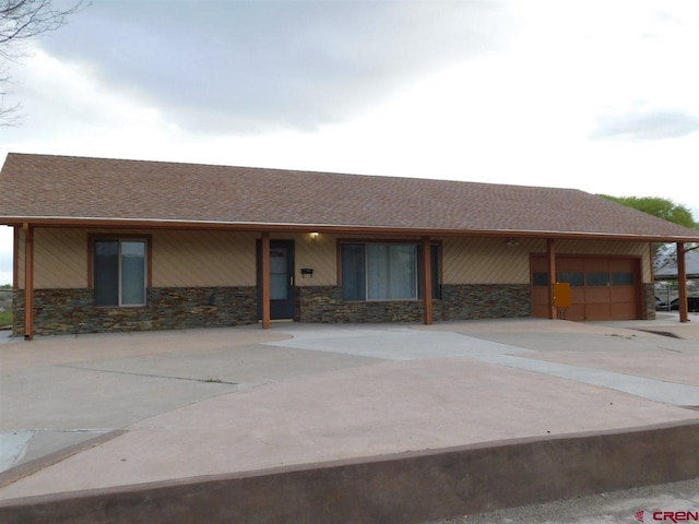 view of front of house featuring an attached garage, stone siding, driveway, and roof with shingles