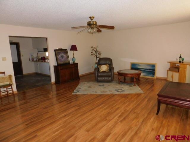 living area featuring a ceiling fan, a textured ceiling, baseboards, and wood finished floors