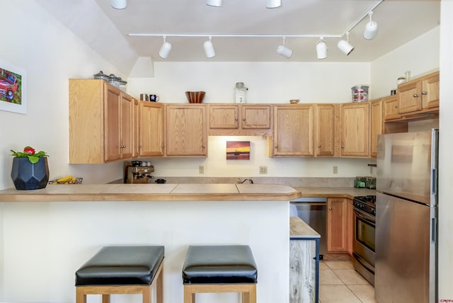 kitchen featuring appliances with stainless steel finishes, a peninsula, light countertops, a kitchen bar, and light tile patterned flooring