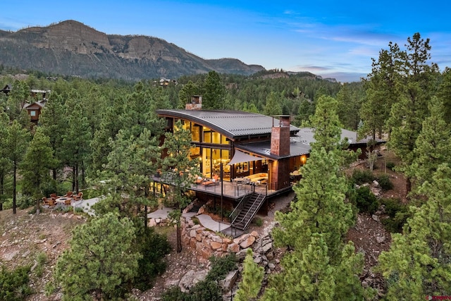 rear view of property with a chimney, metal roof, a mountain view, a forest view, and stairs