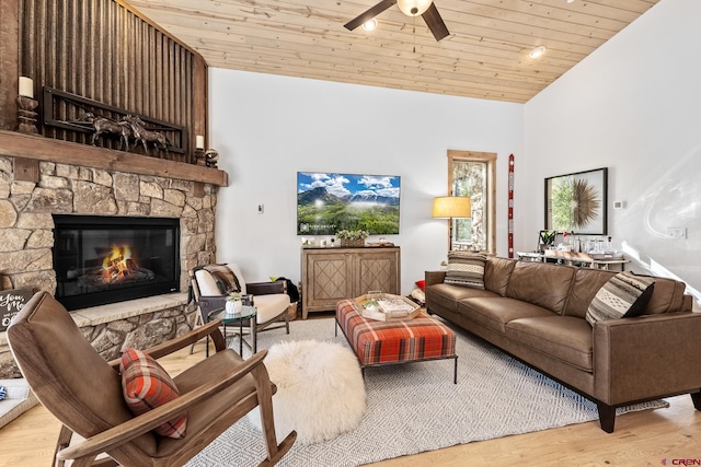 living room with a ceiling fan, wood ceiling, wood finished floors, vaulted ceiling, and a stone fireplace