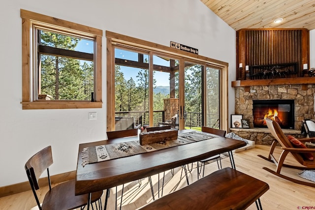 dining space featuring high vaulted ceiling, a stone fireplace, light wood-style flooring, wood ceiling, and baseboards