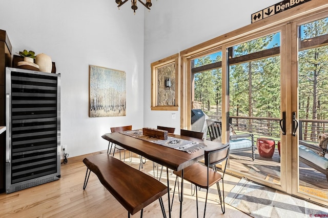 dining space with light wood-style floors, wine cooler, a high ceiling, and baseboards