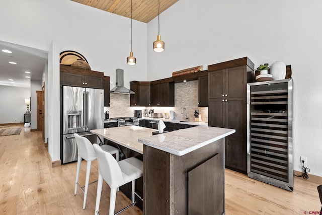 kitchen with wine cooler, a sink, dark brown cabinets, appliances with stainless steel finishes, and wall chimney range hood