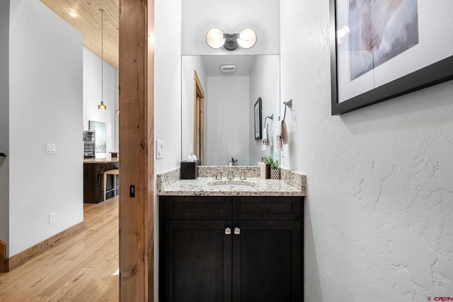 bathroom with a textured wall, wood finished floors, vanity, and baseboards