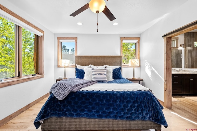 bedroom with recessed lighting, a sink, baseboards, light wood-type flooring, and ensuite bath