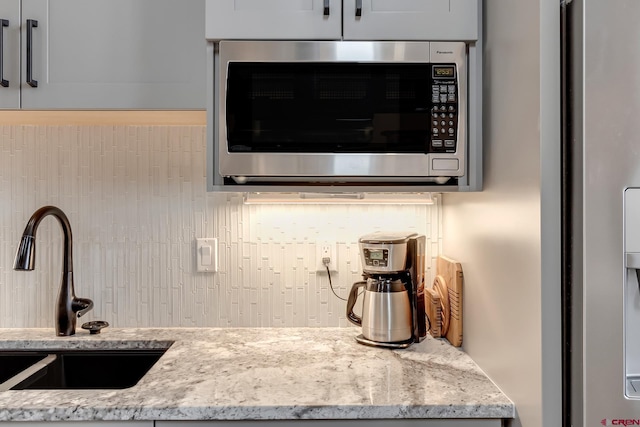 kitchen with tasteful backsplash, appliances with stainless steel finishes, light stone counters, and a sink