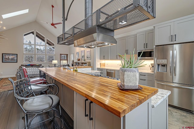 kitchen with a skylight, appliances with stainless steel finishes, open floor plan, gray cabinets, and wooden counters