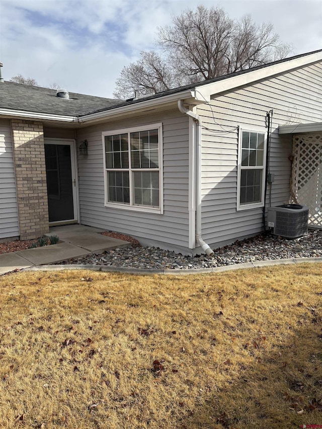 exterior space with brick siding, a lawn, and central AC unit