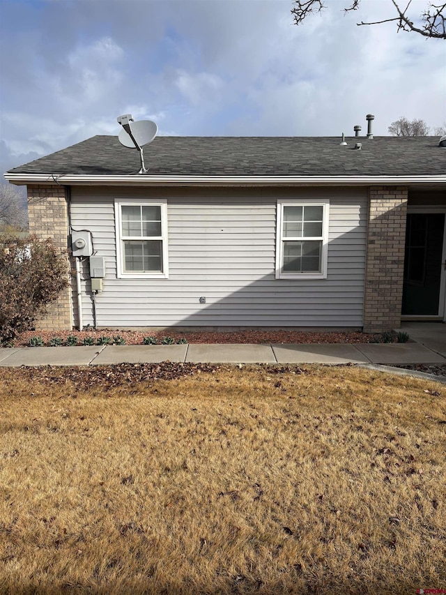 view of home's exterior with a shingled roof, brick siding, and a yard