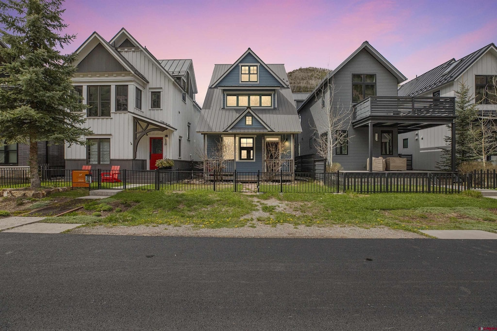 view of front facade with a balcony, a standing seam roof, a fenced front yard, and metal roof