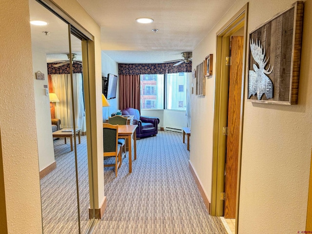 hallway featuring a textured wall, carpet floors, baseboard heating, and baseboards