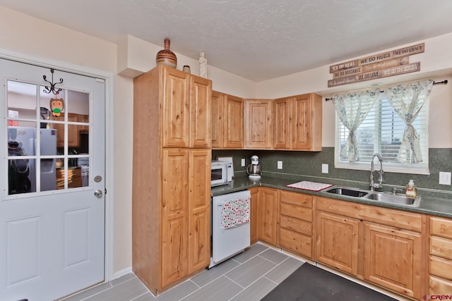 kitchen featuring a textured ceiling, white appliances, a sink, backsplash, and dark countertops