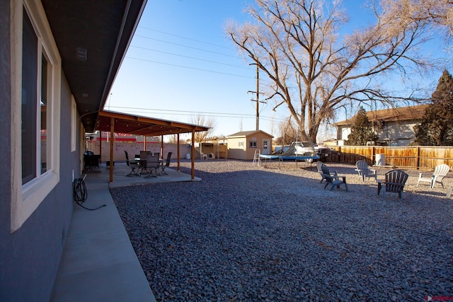 view of yard with a fire pit, a patio, a fenced backyard, an outbuilding, and a trampoline