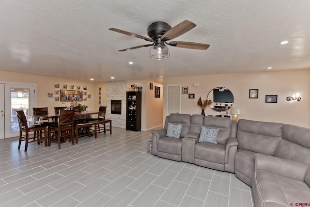 living room featuring ceiling fan, a fireplace, a textured ceiling, and recessed lighting