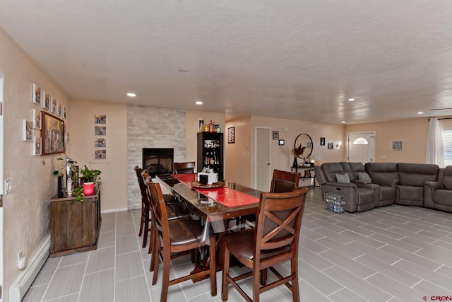 dining space with a baseboard radiator, a fireplace, a textured ceiling, and recessed lighting