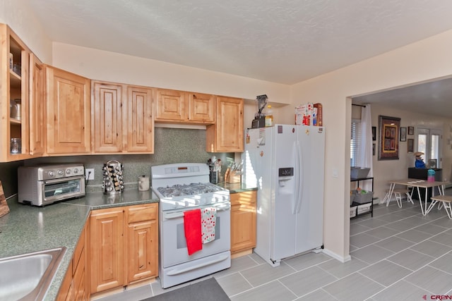 kitchen featuring light tile patterned floors, white appliances, a sink, decorative backsplash, and dark countertops