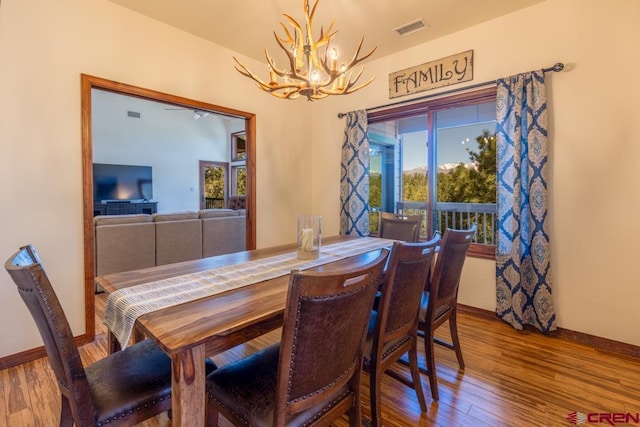 dining room with an inviting chandelier, baseboards, visible vents, and wood finished floors