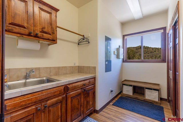 kitchen featuring tile counters, brown cabinetry, a sink, light wood-type flooring, and baseboards