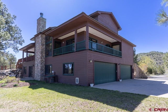 view of side of home with an attached garage, a balcony, concrete driveway, a lawn, and a chimney